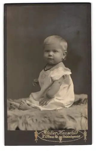 Fotografie Atelier Hauschild, Zittau i. S., Blondes Kind sitzt auf Fellteppich