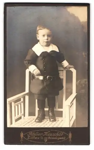 Fotografie Atelier Hauschild, Zittau i. S., Reichenbergstr. 28, Kleiner Junge in eleganter Kleidung auf Stuhl stehend