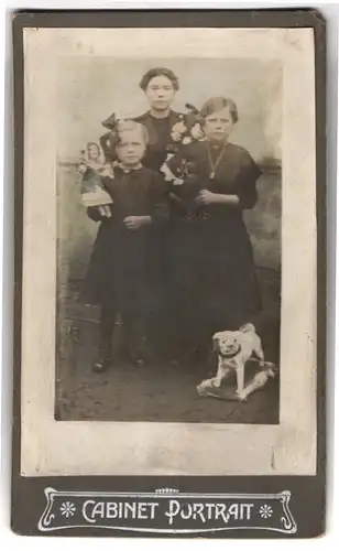 Fotografie unbekannter Fotograf und Ort, drei Schwestern in schwarzen Kleidern mit Puppe und Spielzeug Hund