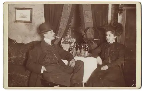 Fotografie unbekannter Fotograf und Ort, Portrait Frau und Mann posieren am Tisch mit Bierflaschen und rauchen Zigarette