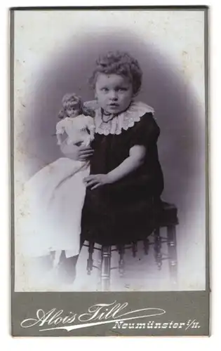 Fotografie Alois Till, Neumünster i. H., kleines Mädchen mit blonden Locken posiert mit Ihrer Puppe im Atelier