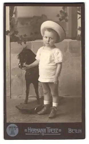 Fotografie Hermann Tietz, Berlin, Portrait niedlicher Knabe im Nicki mit seinem Schaukelpferd, Sommerhut