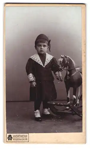 Fotografie Wertheim, Berlin, Rosenthalerstr., Portrait kleiner Knabe im Kleid nebst seinem Schaukelpferd