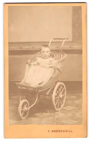 Fotografie F. Kratochwill, Vöslau, Portrait Kleinkind im Kleidchen sitzt im Kinderwagen aus Korbweide