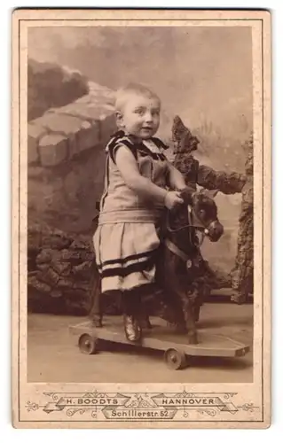 Fotografie H. Boodts, Hannover, Schillerstr. 52, Portrait kleines Mädchen im Kleid auf ihrem Schaukelpferd