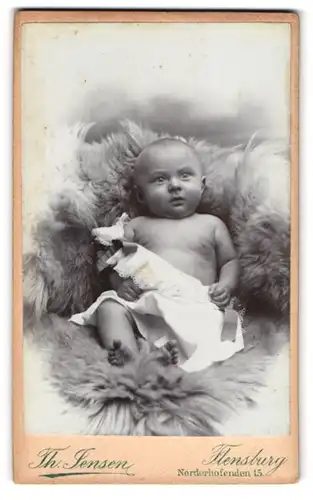 Fotografie Th. Jensen, Flensburg, Norderhofenden 15, Portrait niedliches Baby auf einem Fell liegend