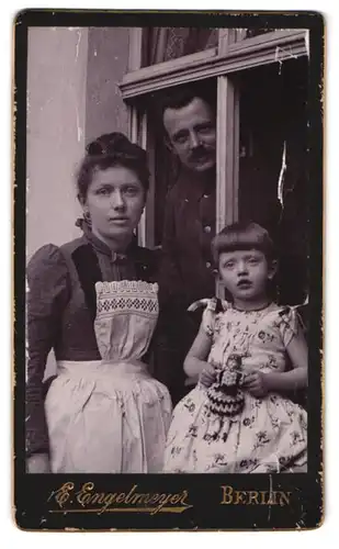 Fotografie E. Engelmeyer, Berlin, Portrait einer Familie mit kleiner Tochter am Fenster stehend