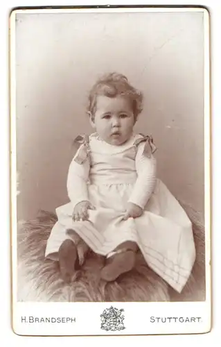 Fotografie H. Brandseph, Stuttgart, Marienstr. 36, Portrait süsses kleines Mädchen im Kleidchen auf Fell sitzend