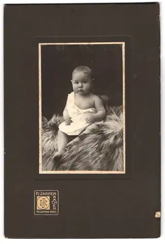 Fotografie R. Jarmer, Aachen, Süsses Kleinkind im Hemd sitzt auf Fell