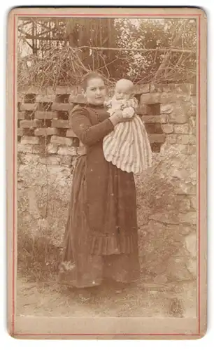 Fotografie unbekannter Fotograf und Ort, Frau im taillierten Kleid mit ihrem Kinde im gestreiften Kleid, Mutterglück