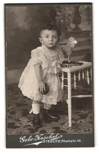 Fotografie Gebr. Koschel, Berlin-Steglitz, Rheinstr. 40, Portrait niedliches Kind im Spitzenkleid mit Spielzeug Schaf