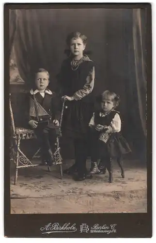 Fotografie A. Birkholz, Berlin, Weidenweg 34, Portrait drei Geschwister in Kleidern und Matrosenanzug mit Segelschiff