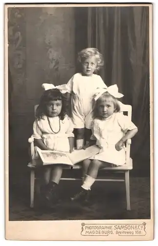 Fotografie Samson & Co., Magdeburg, Breiteweg 168, Portrait drei niedliche Mädchen mit Haarschleife in weissen Kleidern