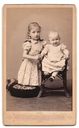 Fotografie Wilh. Lange, Detmold, Portrait zwei niedliche Kinder in hellen Kleidern posiern im Atelier