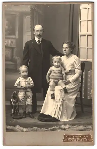 Fotografie Otto Jordan, Hamburg, Winterhuderweg 46, Portrait stolze Eltern mit ihren beiden Kindern, Spielzeugpferd