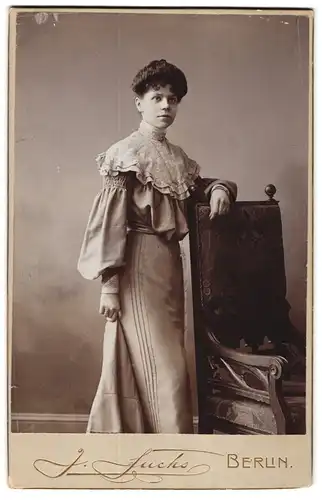 Fotografie J. Fuchs, Berlin, N. Friedrichstr. 108, Portrait junge Dame im Rüschenkleid stehend am Stuhl
