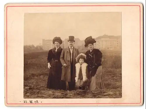 Fotografie unbekannter Fotograf und Ort, Portrait Familie mit Frauen in Winterkleidern und Pelzstola vor der Stadt, 1908