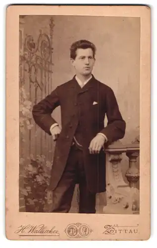 Fotografie H. Walbrecker, Zittau, Breitestr. 9, Eleganter junger Mann in schwarzem Mantel an Ballustrade gelehnt