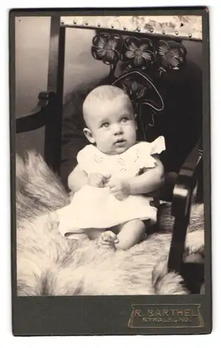 Fotografie Richard Barthel, Stralsund, Frankenstr. 5, Süsses Kleinkind im Kleid sitzt auf Fell