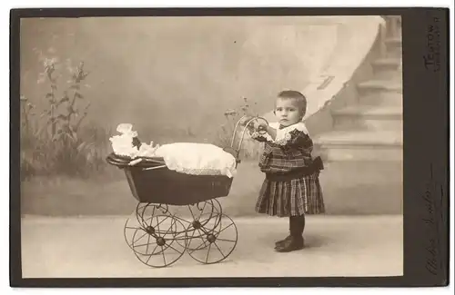 Fotografie Semler, Berlin-Teltow, Lindenstr. 17, Portrait Kleinkind im Kleidchen mit Puppenwagen