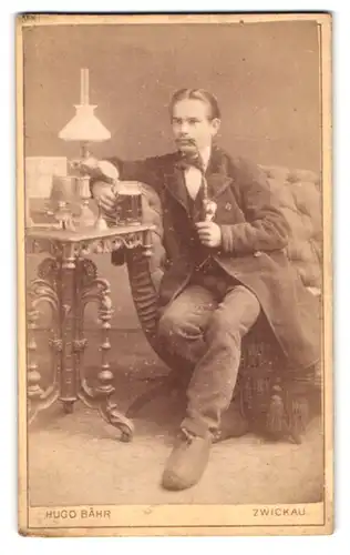 Fotografie Hugo Bähr, Zwickau, Kaiser Wilhelmplatz, Portrait junger Mann im Anzug mit Bierkrug und Pfeife im Atelier