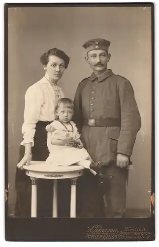 Fotografie A. Lehmann, Berlin, Prinzessinnenstr. 14, Soldat in Feldgrauuniform mit Krätzschen nebst Frau und Kind, Puppe