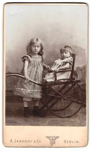 Fotografie A. Jandorf & Co., Berlin, Spittelmarkt 16 /17, Portrait zwei Mädchen in Kleidern mit einem Kinderwagen