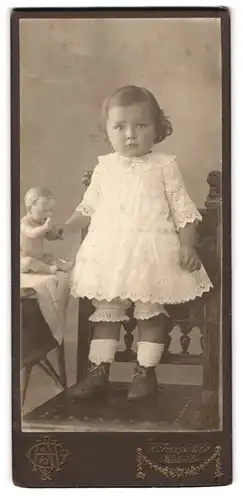 Fotografie H. Joseph & Co., Berlin, Portrait kleines Mädchen Grete Schwarz im weissen Kleidchen mit Puppe auf dem Tisch