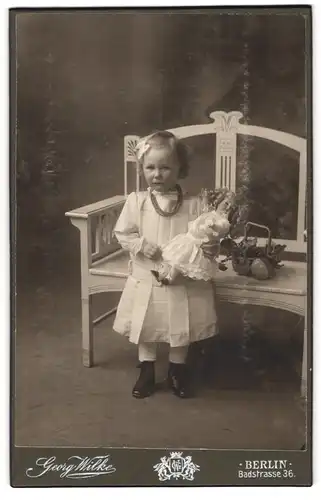Fotografie Georg Wilke, Berlin, Badstr. 36, Portrait blondes Mädchen mit Perlenkette und Puppe im Arm