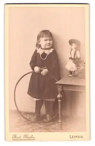 Fotografie Ferd. Thiele, Leipzig, Portrait niedliches Mädchen im Kleid mit Perlenkette und Puppe auf dem Tisch