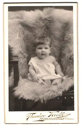 Fotografie Theodor Kratz, Friedrichsfeld, Portrait süsses Kleinkind auf einem Fell sitzend