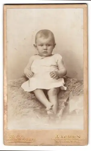 Fotografie R. Jarmer, Aachen, Friedrich-Wilhelm-Platz 5, Portrait süsses Baby im weissen Kleidchen auf Fell sitzend