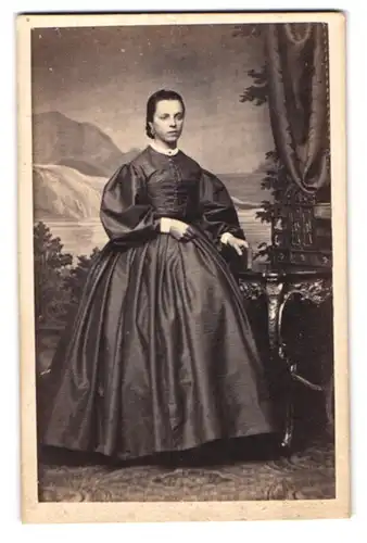 Fotografie A. Tannhof, Lübeck, Portrait junge Dame im reifrock Kleid stehend am Sekretär