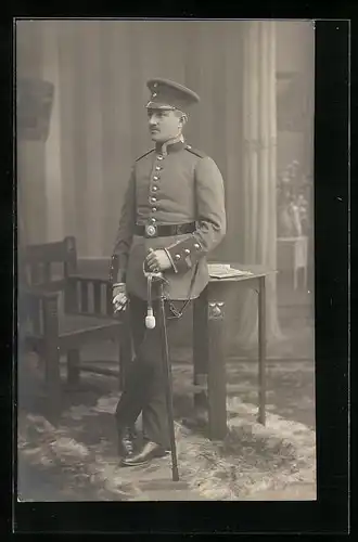 AK Soldat in Uniform mit Säbel und Schirmmütze an einem Tisch lehnend, Uniformfoto