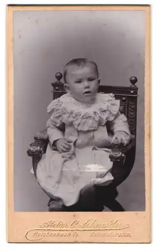 Fotografie Carl Schneider, Reichenbach, Kleinkind im Rüschenkleid sitzt auf Holzstuhl