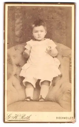 Fotografie G. H. Roth, Bischwiller, Metzgerstrasse 25, Kleinkind in Weiss steht auf altem Sessel