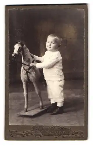 Fotografie Adolf Haynn, Berlin, Frankfurter Allee 92, Portrait niedlicher Knabe in weisser Kleidung mit Schaukelpferd