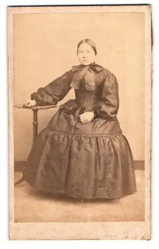 Fotografie unbekannter Fotograf und Ort, Portrait Dame im reifrock Kleid mit Schleife sitzend am Tisch