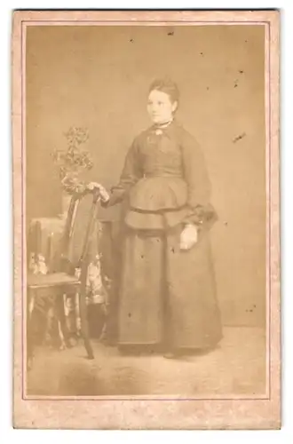 Fotografie unbekannter Fotograf und Ort, Portrait junge Frau im Biedermeierkleid an einen Stuhl gelehnt