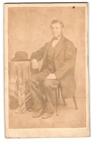 Fotografie unbekannter Fotograf und Ort, Portrait junger Mann im Anzug mit Fliege und Melone auf dem Tisch
