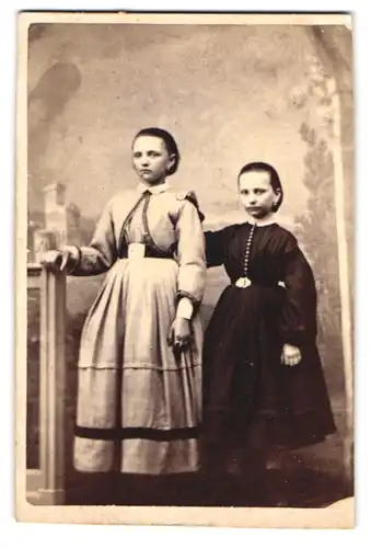 Fotografie unbekannter Fotograf und Ort, Portrait zwei niedliche Mädchen in Biedermeierkleidern posieren im Atelier