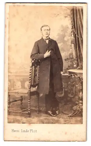 Fotografie Herm. Linde, Lübeck, Johannisstr. 31, Portrait Wilhelm Brandt im Anzug mit Mantel