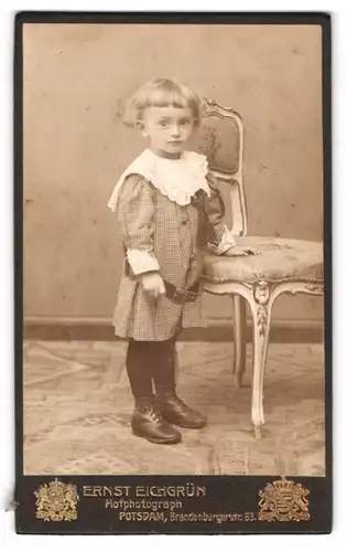 Fotografie Ernst Eichgrün, Potsdam, Brandenburgerstr. 63, Kind im karierten Kleid lehnt am Stuhl