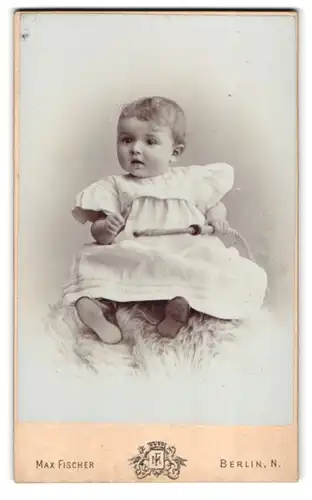 Fotografie Max Fischer, Berlin-N., Invaliden-Str. 16, Kleinkind im Kleid mit Peitsche sitzt auf Fell