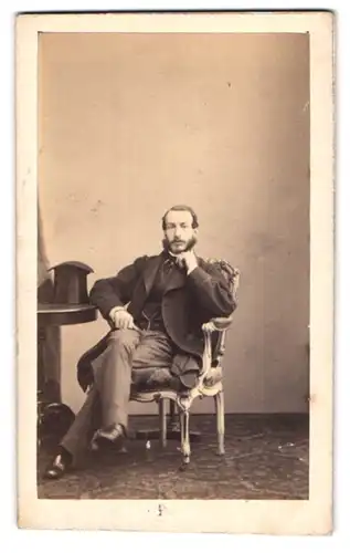 Fotografie H. Geruzet, Bruxelles, Rue del`Ecuyer 27, Portrait Mann im Anzug sitzend am Tisch nebst Zylinder