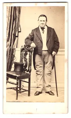 Fotografie unbekannter Fotograf und Ort, Portrait älterer Herr im Anzug mit Stock auf Stuhllehne gestützt, Zylinder