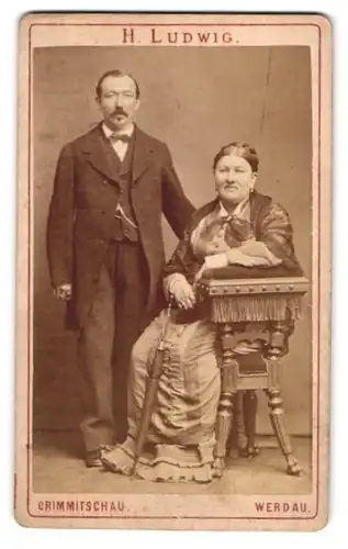 Fotografie H. Ludwig, Crimmitschau, Portrait älteres Paar in zeitgenössischer Kleidung auf einem Gründerzeit Stuhl