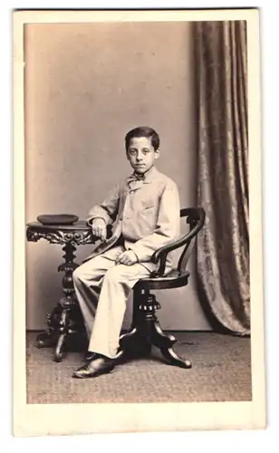 Fotografie Albert Grundner, Berlin, Leipzigerstr. 50, Portrait junger Knabe im hellen Anzug mit Mütze auf dem Tisch