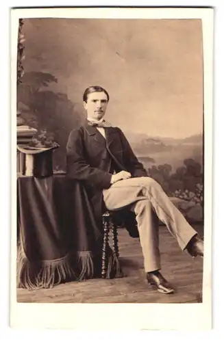 Fotografie Fototgraf und Ort unbekannt, Portrait junger Mann im hellen Anzug mit Zylinder auf dem Tisch