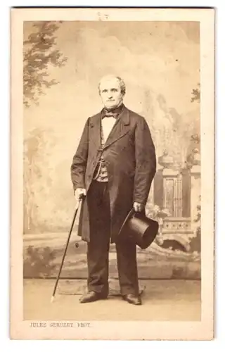 Fotografie Jules Geruzet, Bruxelles, rue del`Ecuyer 27, Portrait Mann im Anzug mit Stock und Zylinder vor Studiokulisse